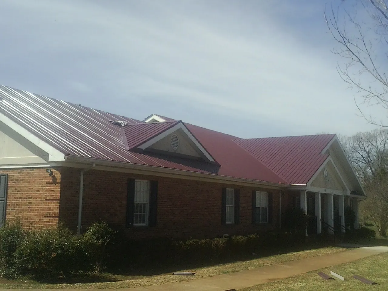 Red metal roof with gabled entries on a long brick building, from a Hail Damage Roof Repair job in Banco