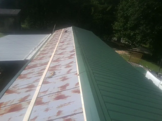 Old rusted panels beside newly installed green metal roofing — Wind Damage Roof Repair by Roofing Brothers in Banco