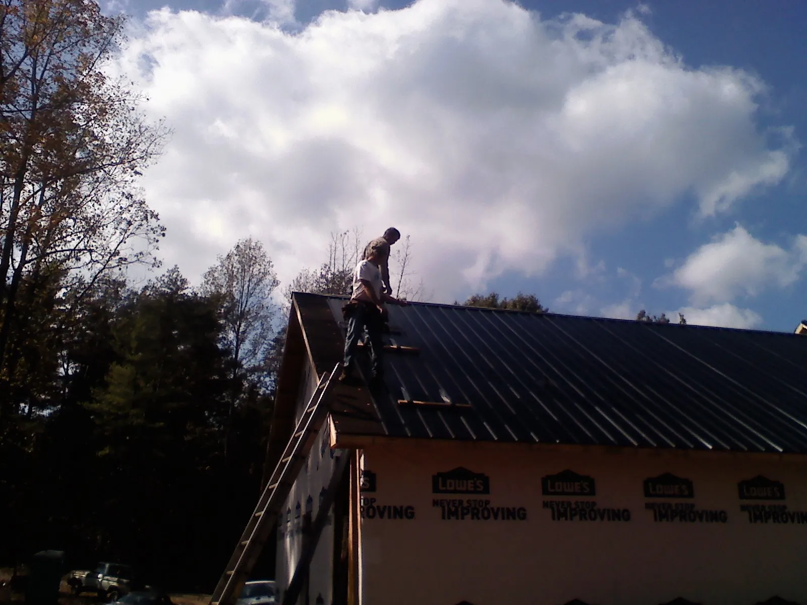 Roofer fastening dark metal panels high against a cloudy sky, from a Roof Inspection job in Banco
