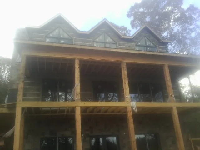 Dormers and porch framing on a large log home under construction — Roof Coating work by our crew in Banco