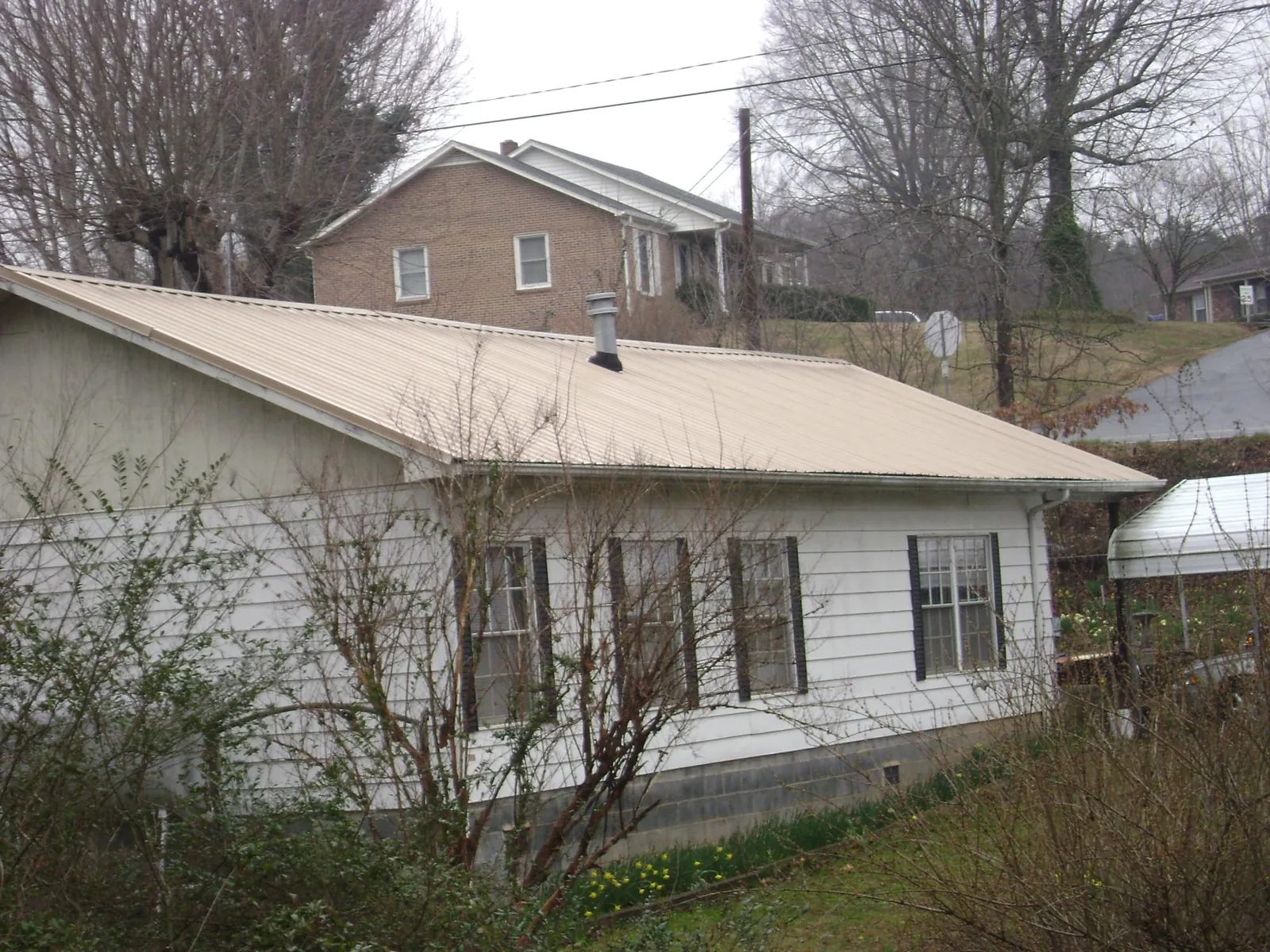Tan metal roof on a white sided house set into a hillside — Commercial Roofing by Roofing Brothers in Banco