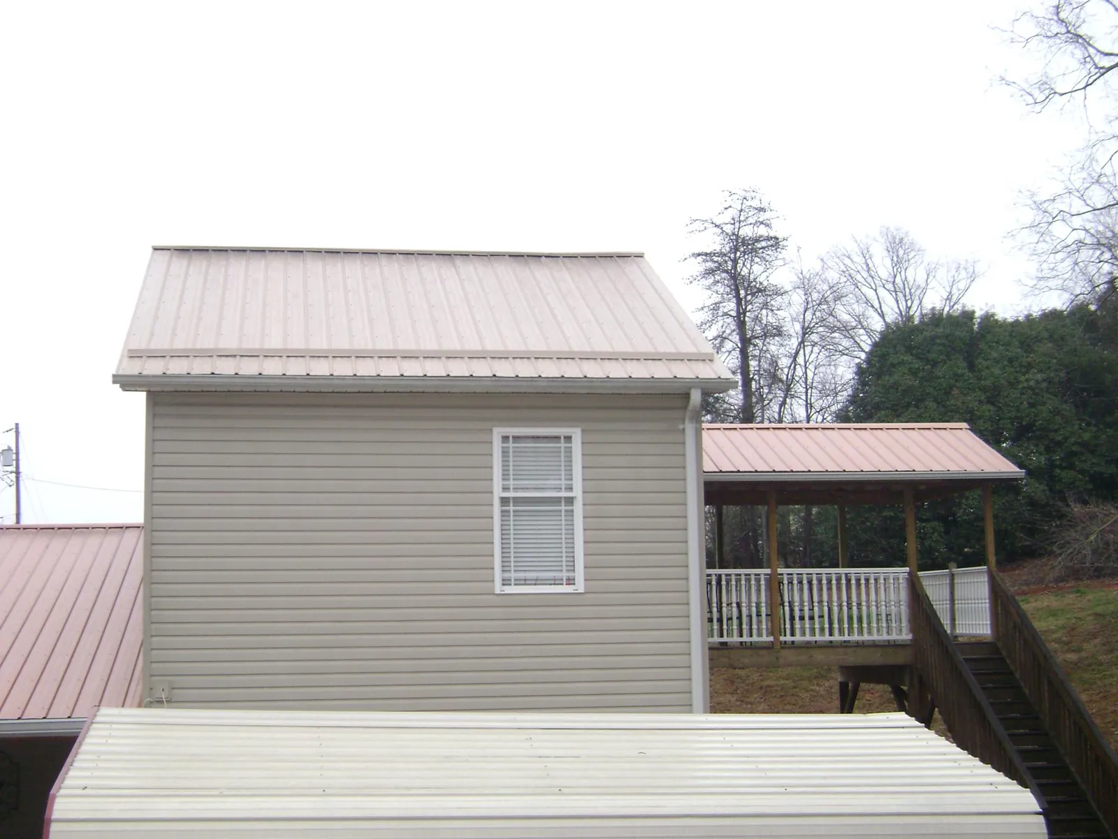Tan metal roofs on a two story addition and attached porch, from a Roof Replacement job in Banco